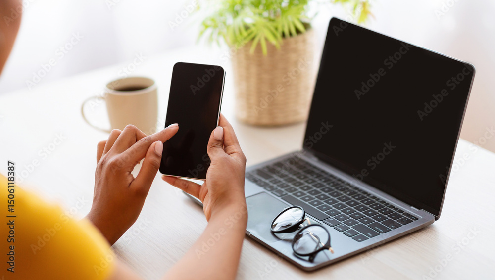 Leinwandbilder Workplace And Workspace. Over The Shoulder View Of Unrecognizable Black Lady Holding Mobile Phone With Blank Empty Screen For Mock Up Template, Sitting At Table With Computer, Plant And Coffee