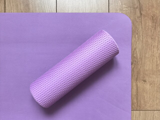 Top view of purple myofascial release roller on fitness yoga mat lying on wooden floor. Sports equipment for fitness, massage and healthy lifestyle