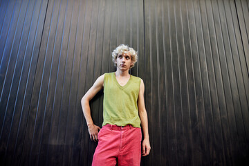 Young adult in casual summer outfit posing against a black wall in urban setting