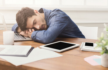 Fototapeta premium Sleep at work. Tired, overworked businessman napping at workplace in modern office interior, copy space