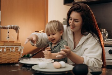 Happy toddler playing with flour and eggs while mother helps in cozy kitchen filled with warmth and laughter gentle parenting love bonding cooking time and sensory joy during sunny morning
