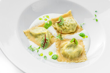 Ravioli with spinach and ricotta cheese with sour cream in plate isolated on white background. Vegetarian dishes, top view, close up