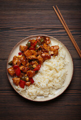 Steaming Chinese kung pao chicken with rice, veggies, and peanuts in spicy sauce. Top view on wooden background. Perfect for lunch or dinner