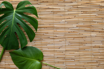 flatlay of two monstera leaves on straw reed shade surface with a space for text
