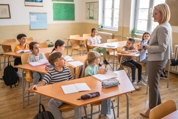 mature woman teacher stand in colorful classroom and teach a lesson
