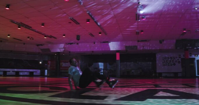 Man attempting to do backwards, crouching trick on roller blades then falls - wide, steady cam shot
