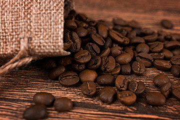 Black coffee foil packaging bag on wooden table top view. Spilled beans flat lay concept. Room for text.