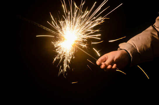 Girl hand holding sparkler, glowing firework, celebration moment, festive lights,close up.