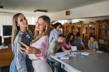 two females student take a self portrait on cellphone in library