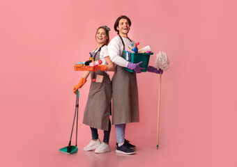 Cleaning Services Concept. Happy young couple holding lots of detergents, posing over pink...