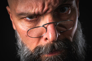 Funny close-up portrait of a quirky bald man with a long gray beard and eyeglasses, making a silly face. Concept of eccentricity, humor, and expressive personality.