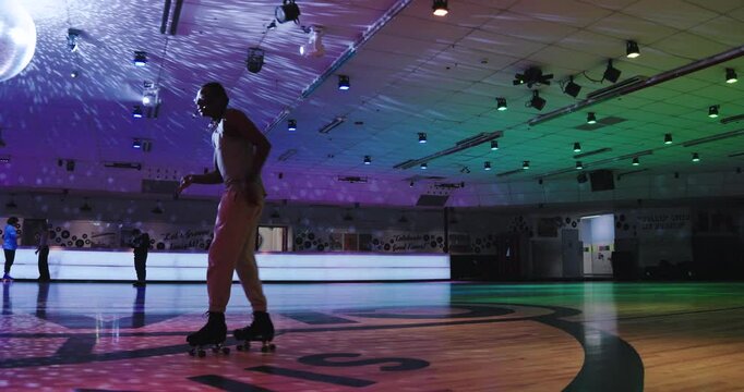Cinematic silhouette of young, professional roller skater skating across floor near disco ball lights - steady cam, side shot 