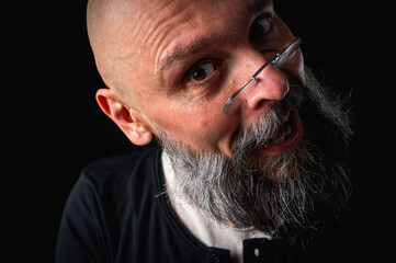 Funny close-up portrait of a quirky bald man with a long gray beard and eyeglasses, making a silly face. Concept of eccentricity, humor, and expressive personality.