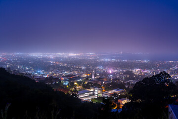 Night view of a city with a bridge in the distance under a purple sky.