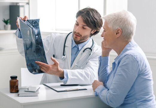MRI examination. Doctor showing x-ray scans of head to senior female patient