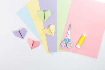 Craft supplies setup with pastel paper sheets, folded origami hearts, glue, and scissors. Perfect...