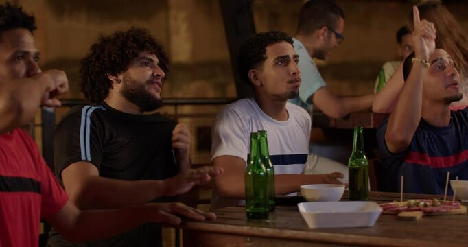 Friends sitting in a bar watching the football match cheering for their team.