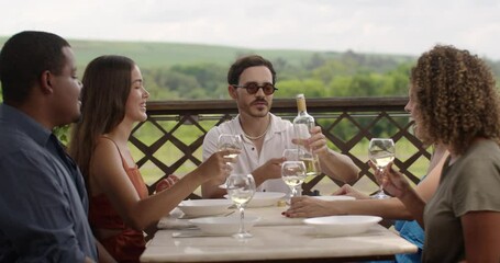 Young man serving wine to his friends sitting at the table at fun outdoor lunch. - Powered by Adobe