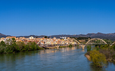 Picturesque view of a bridge spanning a river, with a town and mountains in the background.