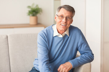 Fototapeta premium Happiness In Old Age. Positive Elderly Gentleman Smiling Looking At Camera Sitting On Sofa At Home.