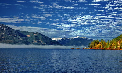 Porteau Cove Provincial Park. Sunny winter day, sea and mountains. . Snow covered mountain range on background Against the beautiful cloudy sky