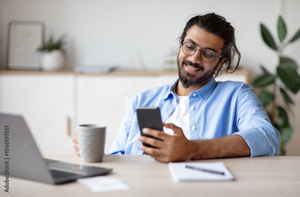 Poster smiling indian employee using smartphone and having coffee in office, enjoying break at work, textin