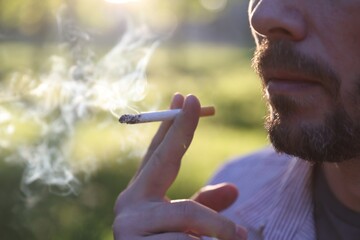 Man smoking cigarette outdoors on sunny day, closeup