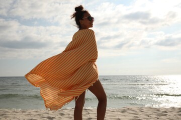 Beautiful African American woman with beach towel on seashore