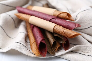 Tasty fruit leather rolls on white tiled table, closeup