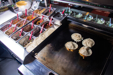 Tacos being cooked on a griddle with assorted fillings beside them, exemplifying the fresh cooking style of traditional street tacos in a bustling environment.