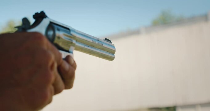Person holding revolver and firing at outdoor shooting range close-up of gun
