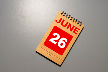 Hand holding a wooden block calendar with the date June 26 on green background.