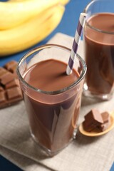 Tasty chocolate milk in glasses, pieces and bananas on table, closeup