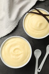 Tasty vanilla pudding with pods and spoons on black table, flat lay