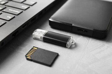 Flash drive, SD memory card, external hard disk and laptop on gray textured table, closeup