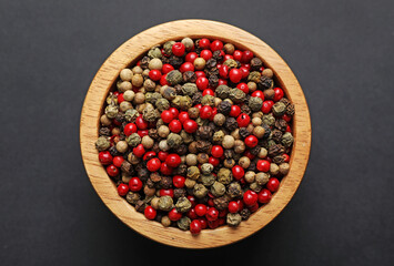 Aromatic peppercorns in bowl on dark table, top view