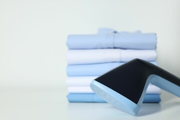 Upright steamer and stack of folded shirts on white table, closeup. Space for text