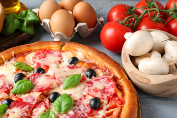 Tasty pizza and ingredients on grey wooden table, closeup