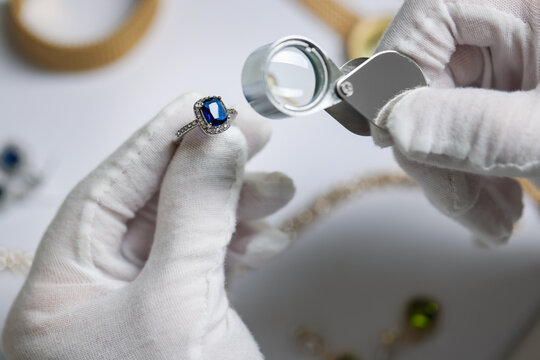 Appraiser with loupe evaluating luxury ring at white table, above view