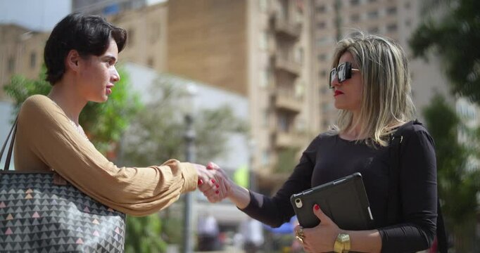 Two women standing in blurred urban background shaking hands closing a deal.