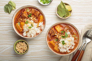Two bowls of rich and flavorful massaman curry are served with beef, potatoes, and fluffy white rice, topped with crunchy peanuts and fresh parsley, a vibrant and aromatic thai dish