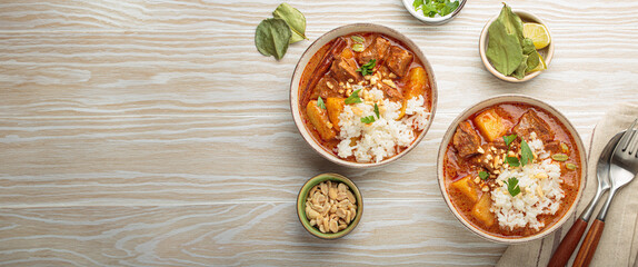 Two bowls of rich and flavorful massaman curry are served with beef, potatoes, and fluffy white rice, topped with crunchy peanuts and fresh parsley, a vibrant and aromatic thai dish