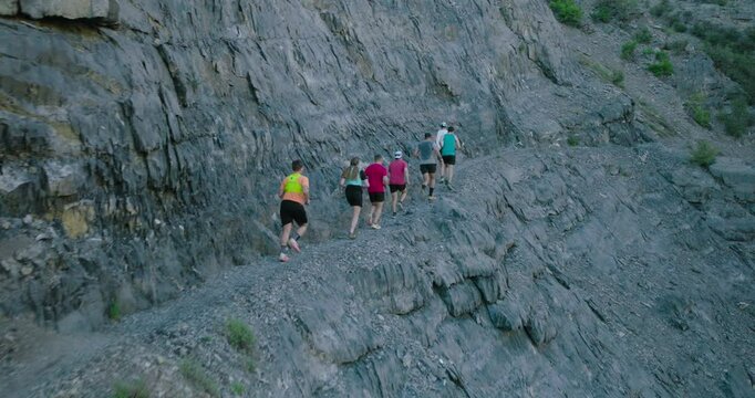 Drone shot following group of runners on rocky mountain path early in the morning