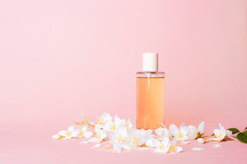 Glass perfume bottle with jasmine flowers on pink background. Beauty and wellness concept. Front view, copy space