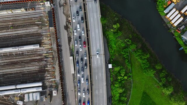 Brooklyn, New York &mdash; Overhead aerial image of Belt Parkway traffic alongside an MTA train yard and Coney Island Creek. Cars move through the highway corridor bordered by dense infrastructure and green