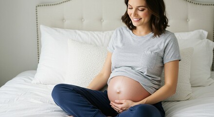 Smiling expectant mother in pajamas sitting cross-legged on a bed with a serene expression and a visible baby bump.