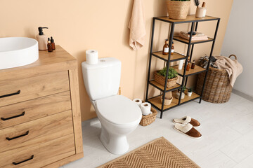 Interior of modern restroom with toilet bowl, shelving unit and chest of drawers with sink near...