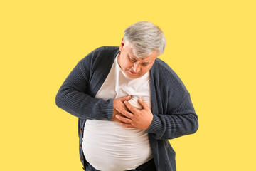Senior man having heart attack on yellow background