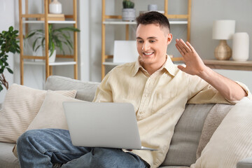 Young man with laptop video chatting on sofa at home
