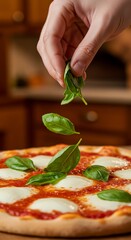 Italian-style Margherita pizza being garnished with fresh basil by hand, kitchen background blurred